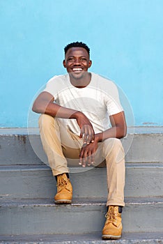 Stylish young man sitting on steps and smiling