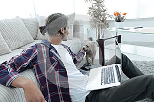 Stylish young man stroking his pet and working on laptop