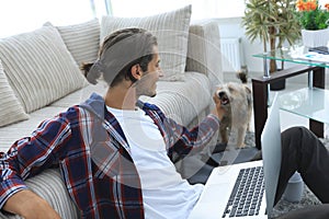 Stylish young man stroking his pet and working on laptop