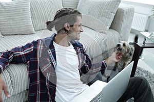 Stylish young man stroking his pet and working on laptop