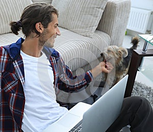 Stylish young man stroking his pet and working on laptop