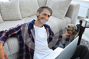 Stylish young man stroking his pet and working on laptop