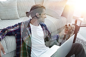 Stylish young man stroking his pet and working on laptop