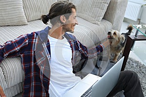 Stylish young man stroking his pet and working on laptop