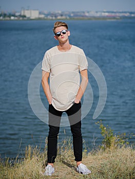 Stylish young man in sunglasses. Tall, cool guy walking near the river on a blurred background. College style concept.