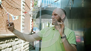 Stylish young man taking selfie with smartphone camera showing ok hand gesture posing outdoors