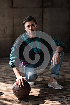 stylish young man in vintage windcheater with basketball ball sitting squats photo