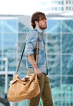 Stylish young man walking with travel bag