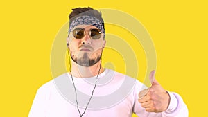 Stylish Young Man Wearing Fashionable Glasses and Bandana, Listens Music on Headphones and Shows Thumb Up. Yellow