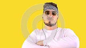 Stylish young man in a white sweater and fashionable glasses stands and listens to music on a yellow background isolated