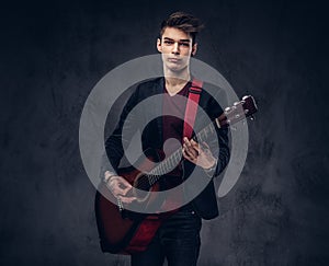 Stylish young musician with stylish hair in elegant clothes, playing on an acoustic guitar.