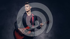 Stylish young musician with stylish hair in elegant clothes, playing on an acoustic guitar.