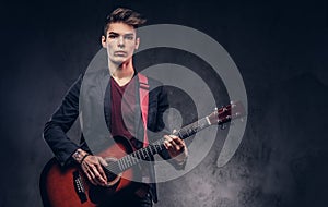 Stylish young musician with stylish hair in elegant clothes, playing on an acoustic guitar.