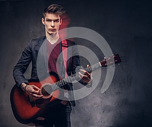 Stylish young musician with stylish hair in elegant clothes, playing on an acoustic guitar.