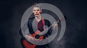 Stylish young musician with stylish hair in elegant clothes, playing on an acoustic guitar.