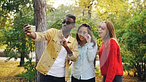 Stylish young people man and women are taking selfie wearing sunglasses posing and smiling holding smartphone during