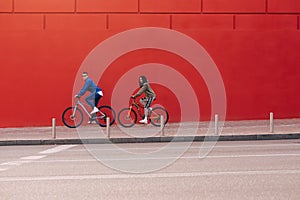 Stylish young people walk on a bicycle on a background of a red wall on the city streets. Athletic couple of cyclists ride on a