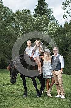 Stylish young ranch family, father, mother and two girls daughters riding a horse in a park or forest on a sunny summer