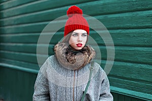 Stylish young Russian girl in fashionable winter clothes standing near a green wooden wall