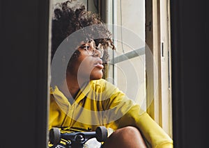 Stylish young sensual black pensive woman sitting near the window with a skateboard