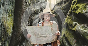 Stylish young traveler girl in hat looking at map, exploring woods