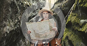 Stylish young traveler girl in hat looking at map, exploring woods