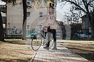 Stylish young woman with bicycle on sunny city park pathway