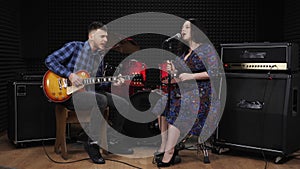 Stylish young woman and man are playing on guitar and singing songs with emotions and movements. Acoustic performance by music ban