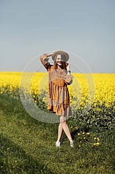 Stylish young woman in straw hat in a field of yellow flowers. Girl in a floral dress