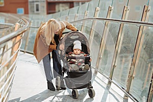 Stylish young woman walking and pushing her baby in stroller on the street