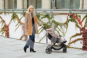 Stylish young woman walking and pushing her baby in stroller on the street.