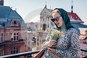 Stylish young woman wearing green retro shawl with sunglasses holding spring flowers. Classic vintage outdoor fashion