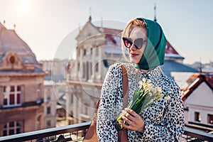 Stylish young woman wearing green retro shawl with sunglasses holding spring flowers. Classic vintage outdoor fashion
