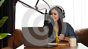 Stylish young woman wearing headphone using condenser microphone and laptop to recording podcast in home studio