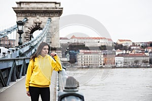 Stylish young woman in yellow hoody posing in the city streets.