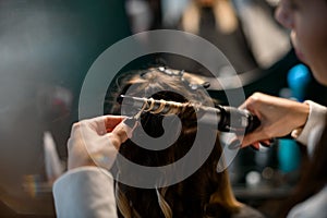 stylist accurate makes curls hairstyle of hair with the curling iron in hairdresser salon, close up