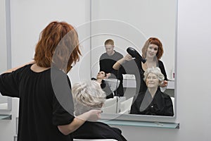 Stylist Blow Drying Senior Woman's Hair In Salon