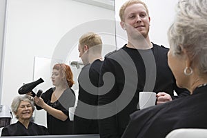 Stylist Blow Drying Senior Woman's Hair In Salon