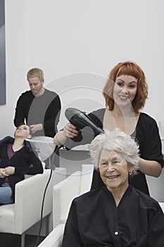 Stylist Blow Drying Senior Woman's Hair In Salon