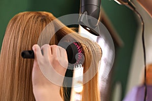 Stylist blow drying woman`s hair in salon