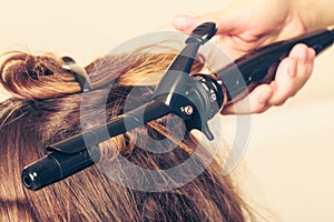 Stylist curling hair for young woman.