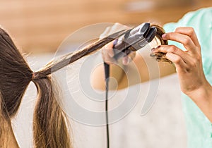 Stylist curling hair for young woman. Girl care about her hairstyle