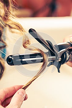 Stylist curling hair for young woman.