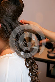Stylist doing curls with irons rod on long brunette hair
