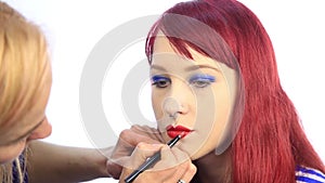 Stylist draws the contour of the model`s lips with a red pencil. make-up artist apply lipstick with brush on a woman`s