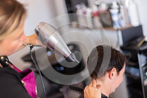 Stylist drying woman hair in hairdresser salon.
