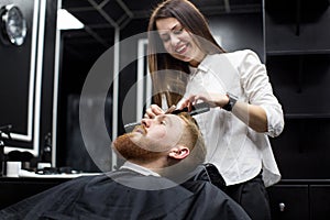 stylist girl shaves beard man in Barbershop.