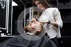 stylist girl shaves beard man in Barbershop.