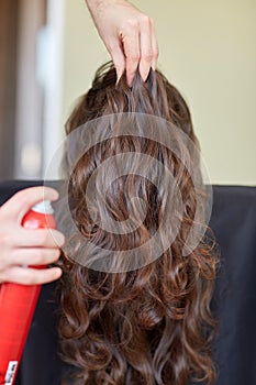 Stylist with hair spray making hairdo at salon