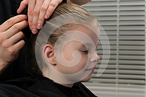 Stylist hairdresser. creates a hairstyle for the evening, little girl, stabs hair with a hairpin, baby smiles